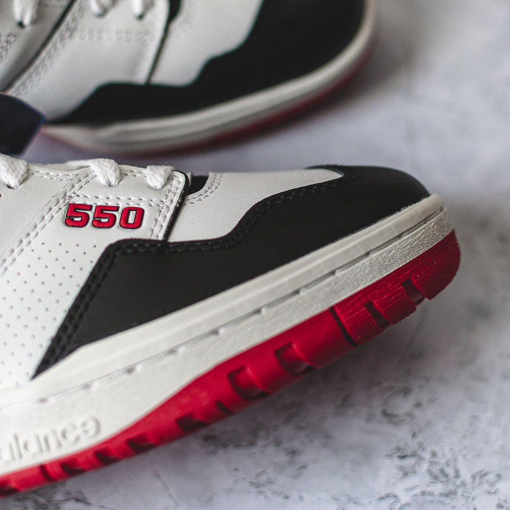 New Balance 550 sneakers in white, red, and black color.